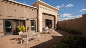 A building with a patio area featuring hexagonal paving, outdoor seating with chairs and tables, and potted plants. - Hampton Inn Oneonta (Oneonta)