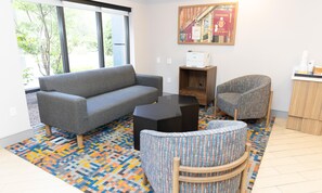 A living room with a grey sofa, a patterned armchair, a black coffee table, and a colorful rug.
