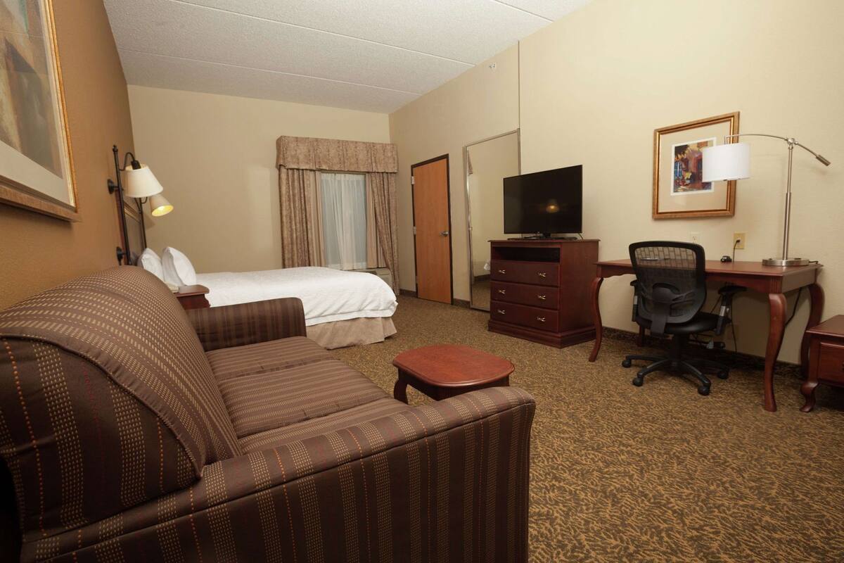 Habitación de hotel con cama, sofá, escritorio con computadora, televisor y lámpara.