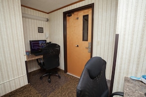 Habitación de hotel con puerta de madera, un escritorio con computadora, una silla de oficina negra y una alfombra estampada.
