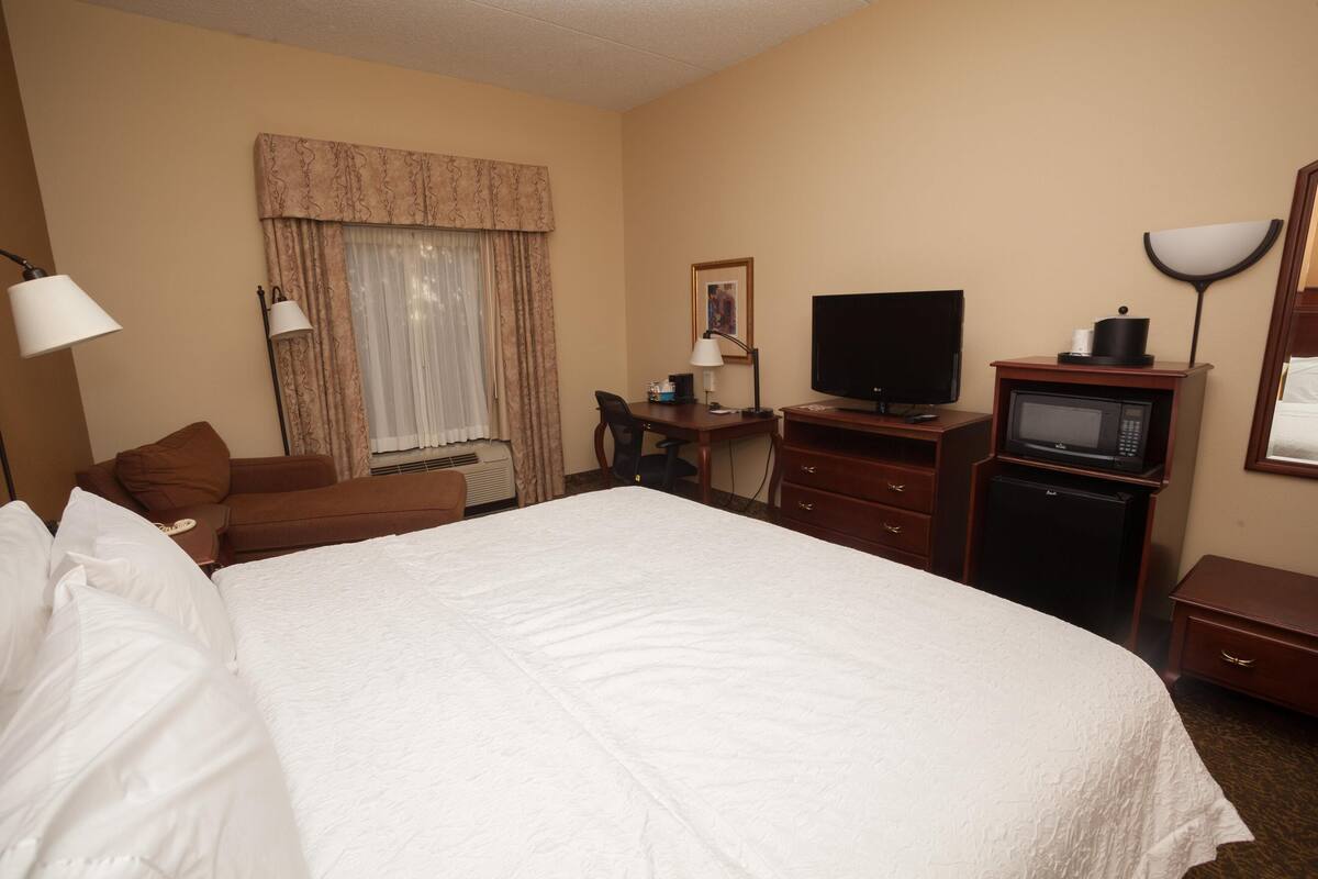 Habitación de hotel con una cama grande, un escritorio con computadora, televisor, microondas y un refrigerador pequeño.