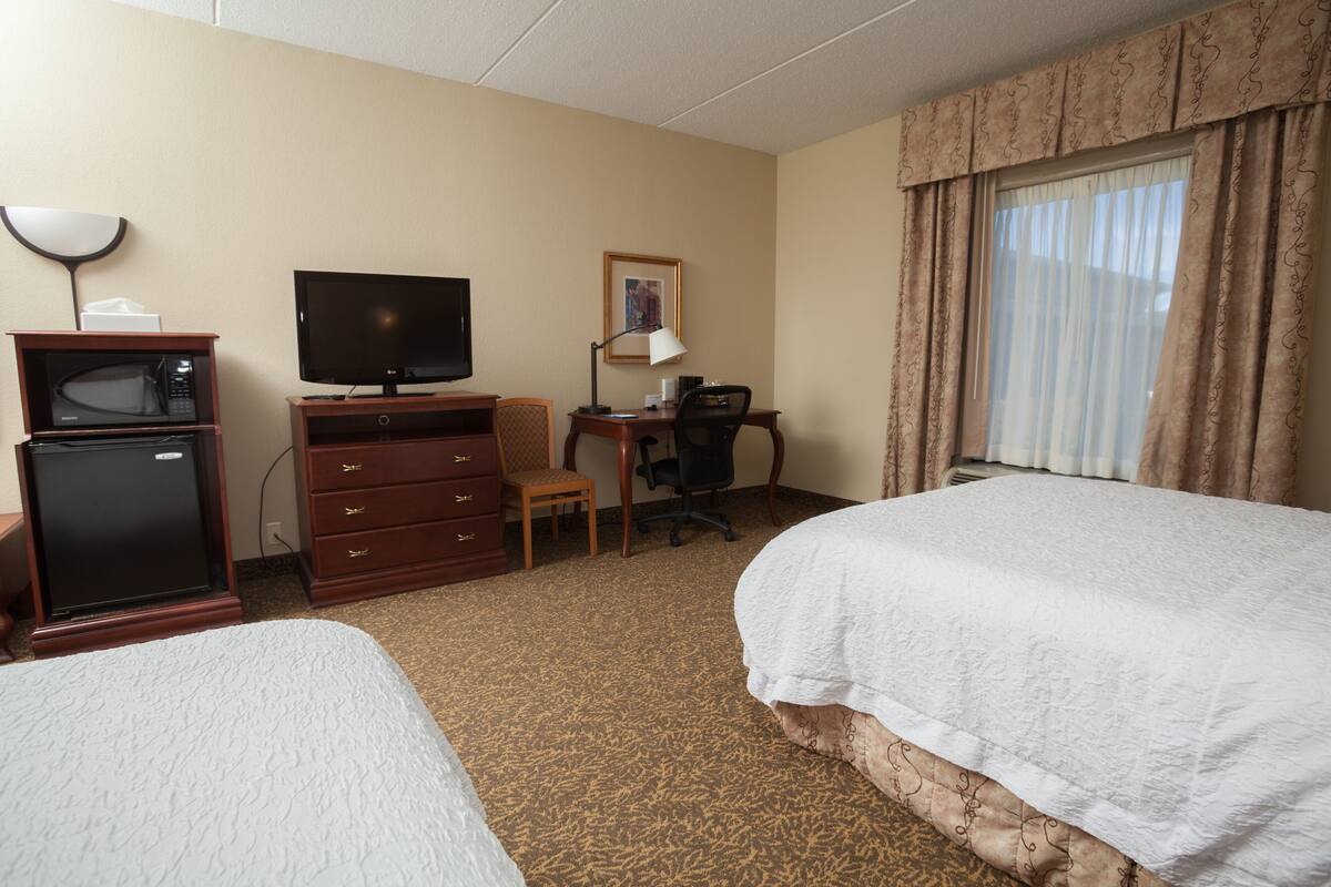Una habitación de hotel con dos camas, un escritorio con silla, televisión, microondas y una lámpara.