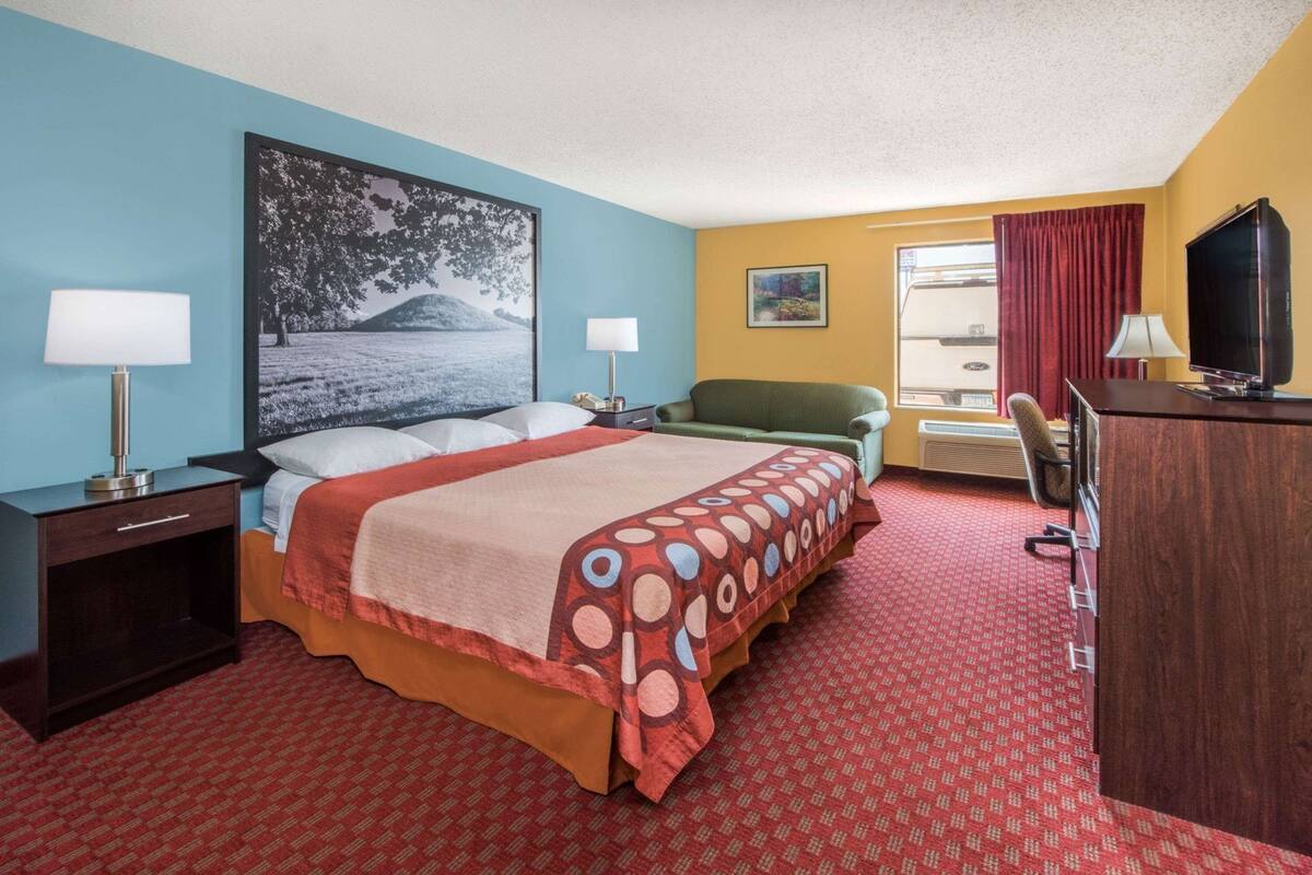 A hotel room with a bed, two bedside tables, a desk with a chair, a television, and a window with curtains.