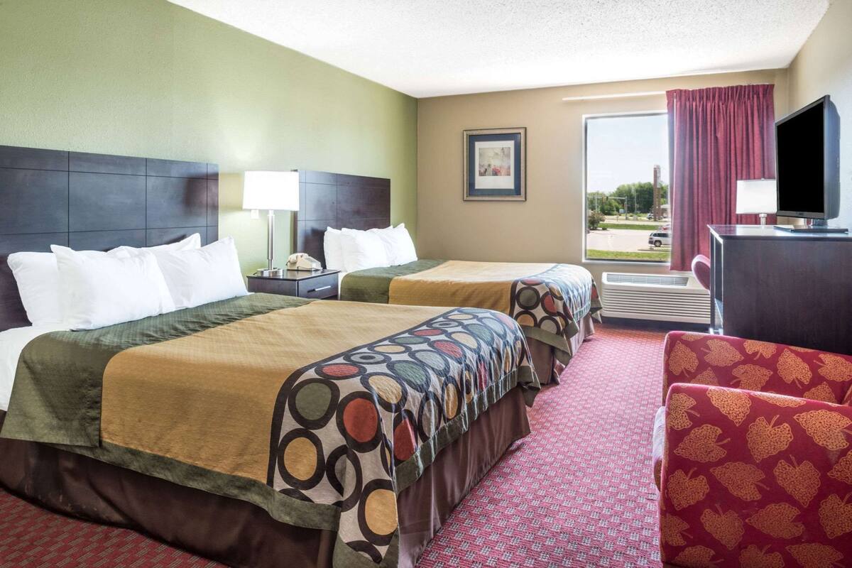 A hotel room with two beds, a desk, a TV, and a window with a view.