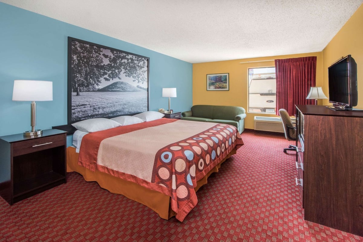 A hotel room with a bed, two bedside tables, a desk with a chair, a television, and a window with curtains.