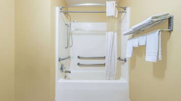 A bathroom with a bathtub, grab bars, a showerhead, and a towel rack with multiple towels.
