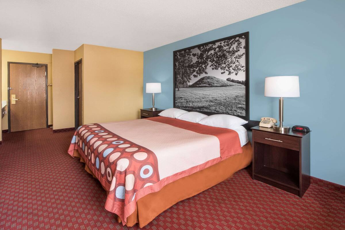 A hotel room with a bed, two bedside tables with lamps, a telephone, and a painting on the wall.