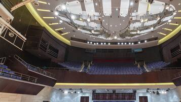 Un ampio auditorium interno con posti a gradinata, un palco centrale e un sistema di illuminazione moderno.