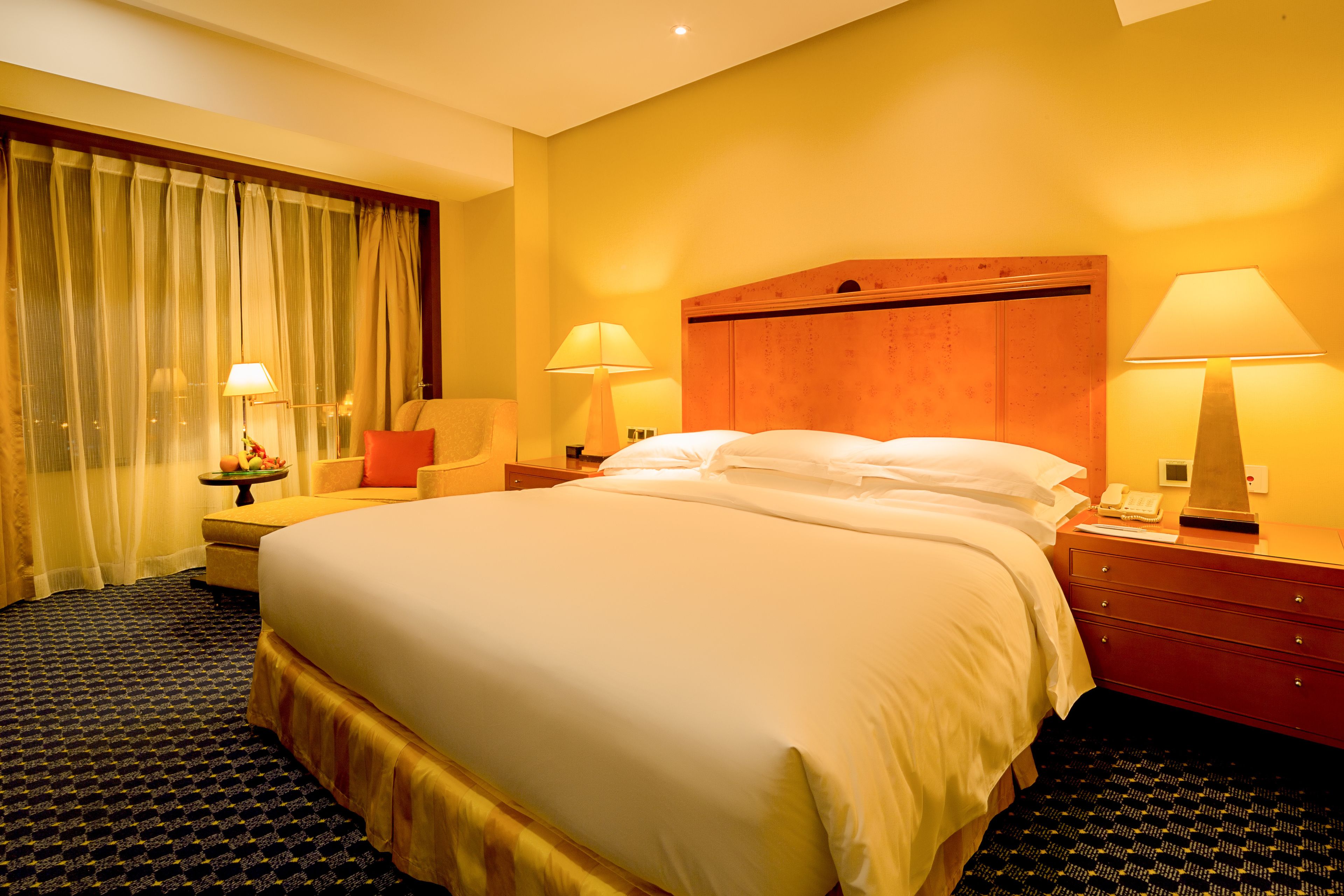 A hotel room with a large bed, two bedside tables with lamps, a nightstand, a chair, and a window with curtains.