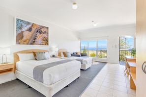 Two large beds with white bedding and gray throw pillows, a large abstract painting, and a balcony with ocean views.