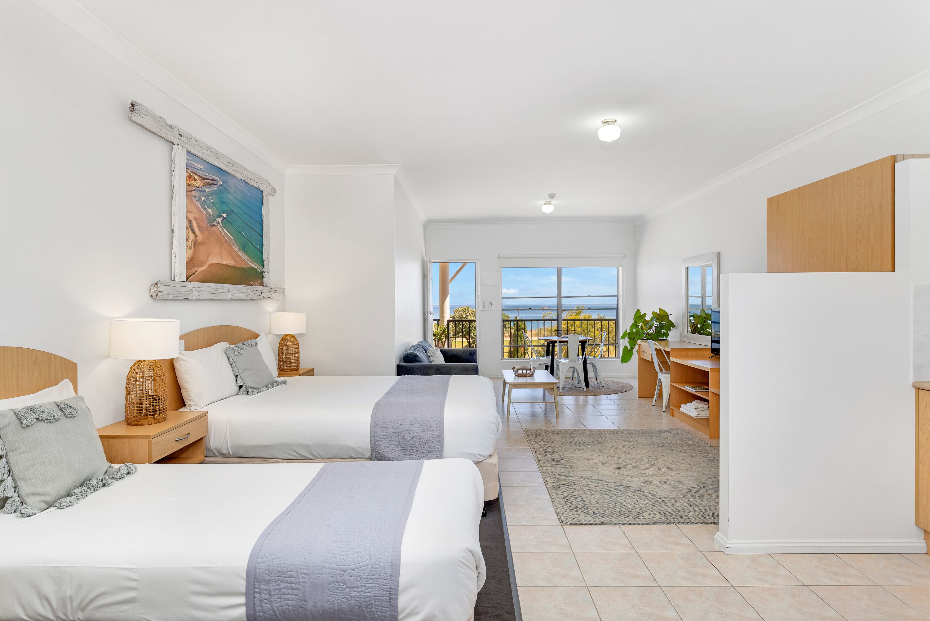 Habitación de hotel con dos camas, un escritorio y un balcón con vistas.