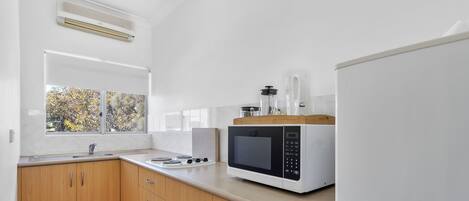 A modern kitchen with wooden cabinets, a white countertop, a built-in microwave, and a window with a view of trees.