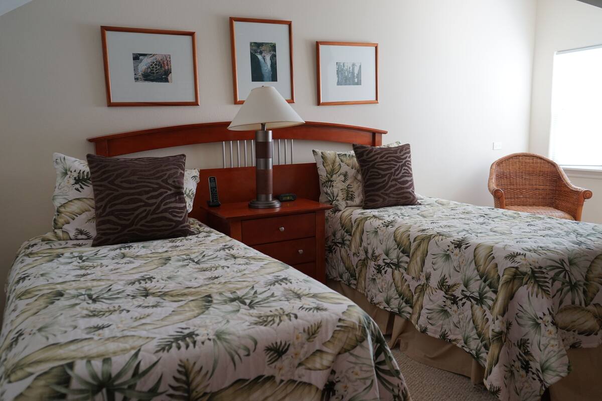 A hotel room with two beds, a nightstand, a lamp, and framed pictures on the wall.