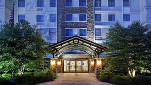 A multi-story hotel with a stone facade, a covered entrance, and an American flag. - Homewood Suites by Hilton Eatontown (Eatontown)