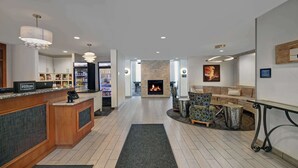 A hotel lobby with a reception desk, a fireplace, seating area, and a dining table. - Homewood Suites by Hilton Eatontown (Eatontown)