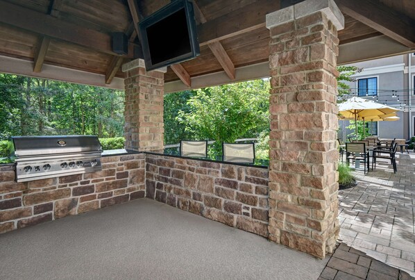 An outdoor patio with a stone wall, a grill, and a TV mounted on the wall.