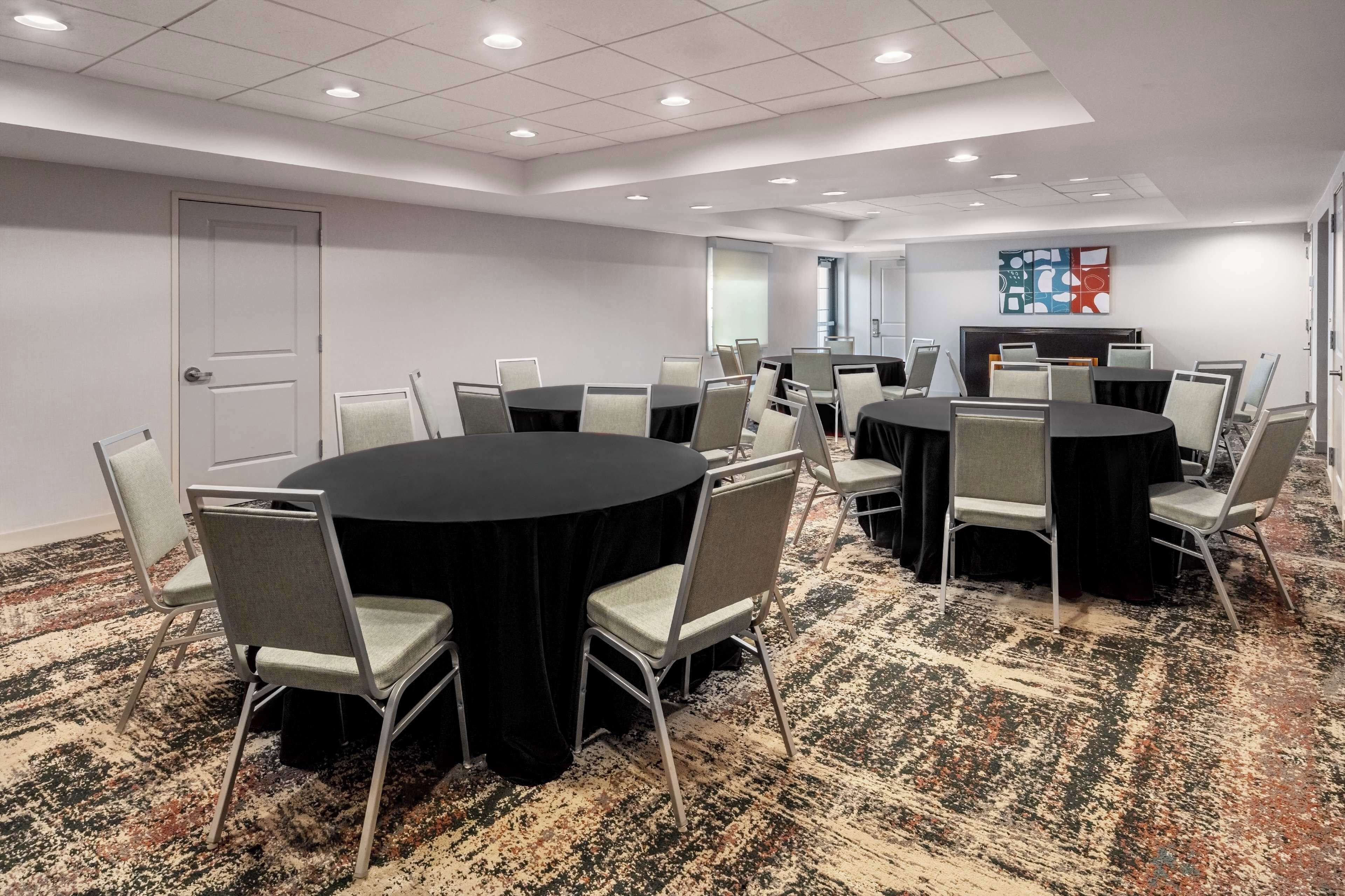Uma sala de conferência com várias mesas redondas e cadeiras, piso coberto de carpete e uma porta.