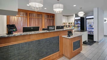 Zona de recepción de un hotel con mostrador de mármol, paneles de madera y una minibar.