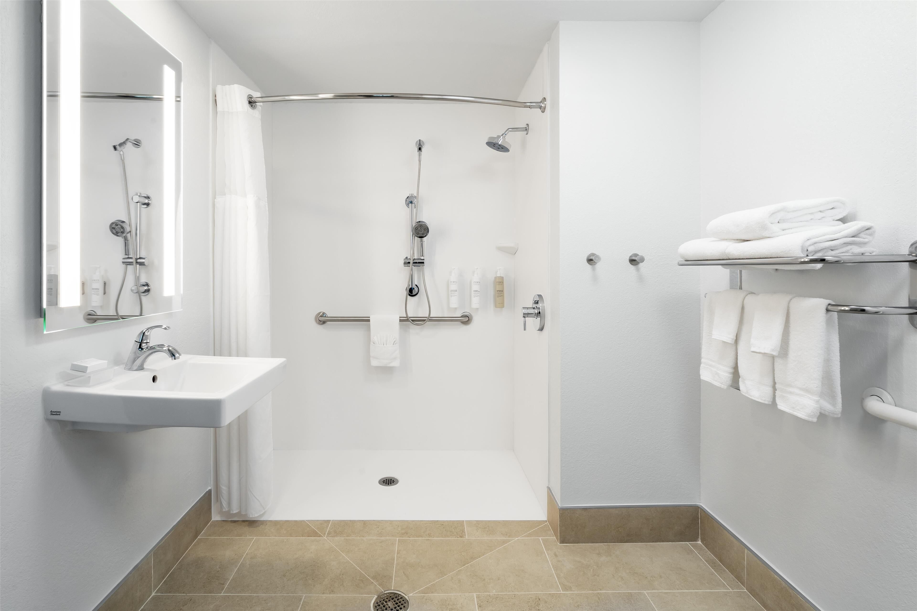 Ein modernes Badezimmer mit einem weißen Waschbecken, einer Dusche mit Glastür und einem Handtuchhalter mit gefalteten Handtüchern.