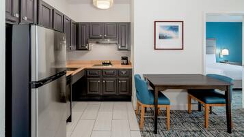 A modern kitchen with dark cabinets, a stainless steel refrigerator, and a dining area with blue chairs.