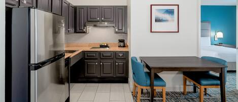 A modern kitchen with dark cabinets, a stainless steel refrigerator, and a dining area with blue chairs.