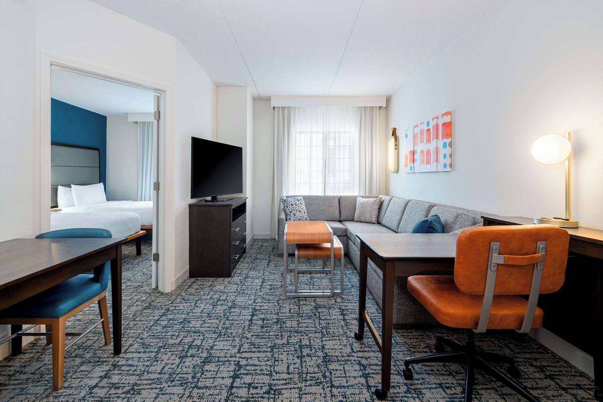 A hotel room with a bed, a desk, a sofa, a TV, and a lamp.