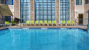 A swimming pool with a stone facade and large windows, surrounded by green chairs. - Homewood Suites by Hilton Eatontown (Eatontown)