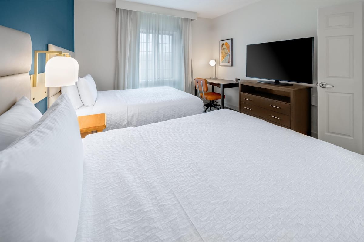 A hotel room with two beds, a desk, a television, and a chair.