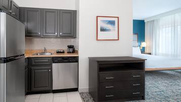Una habitación de hotel compacta con kitchenette, una cama y un cuadro en la pared.