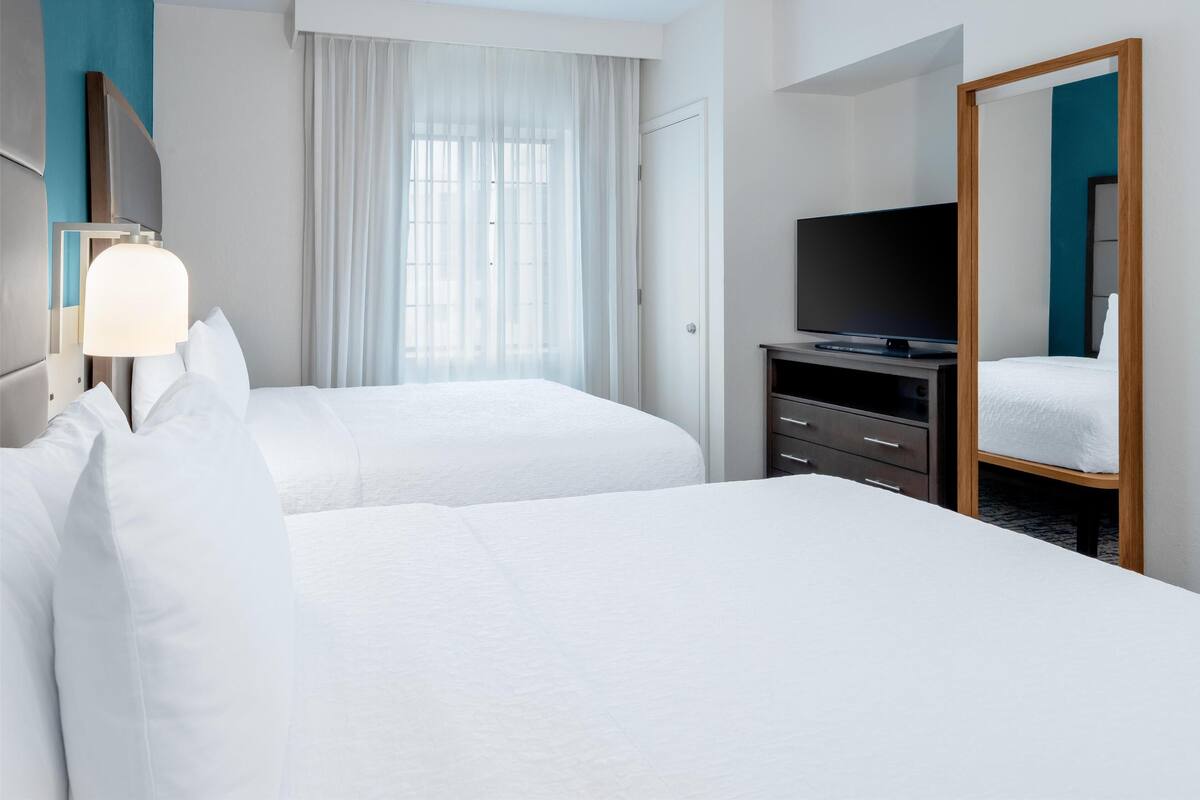 A hotel room with two beds, a TV, a dresser, and a large mirror.
