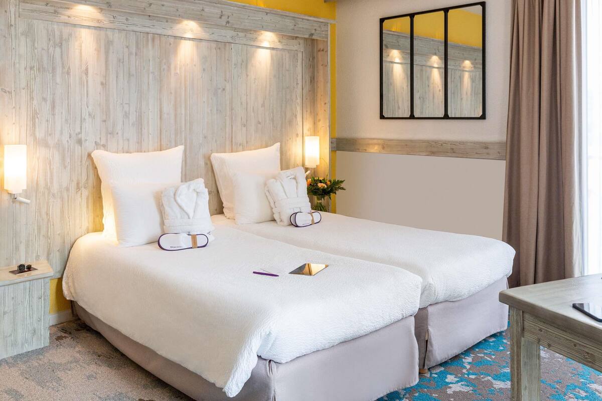 A hotel room with two beds, a wooden headboard, a mirror, and a small table.