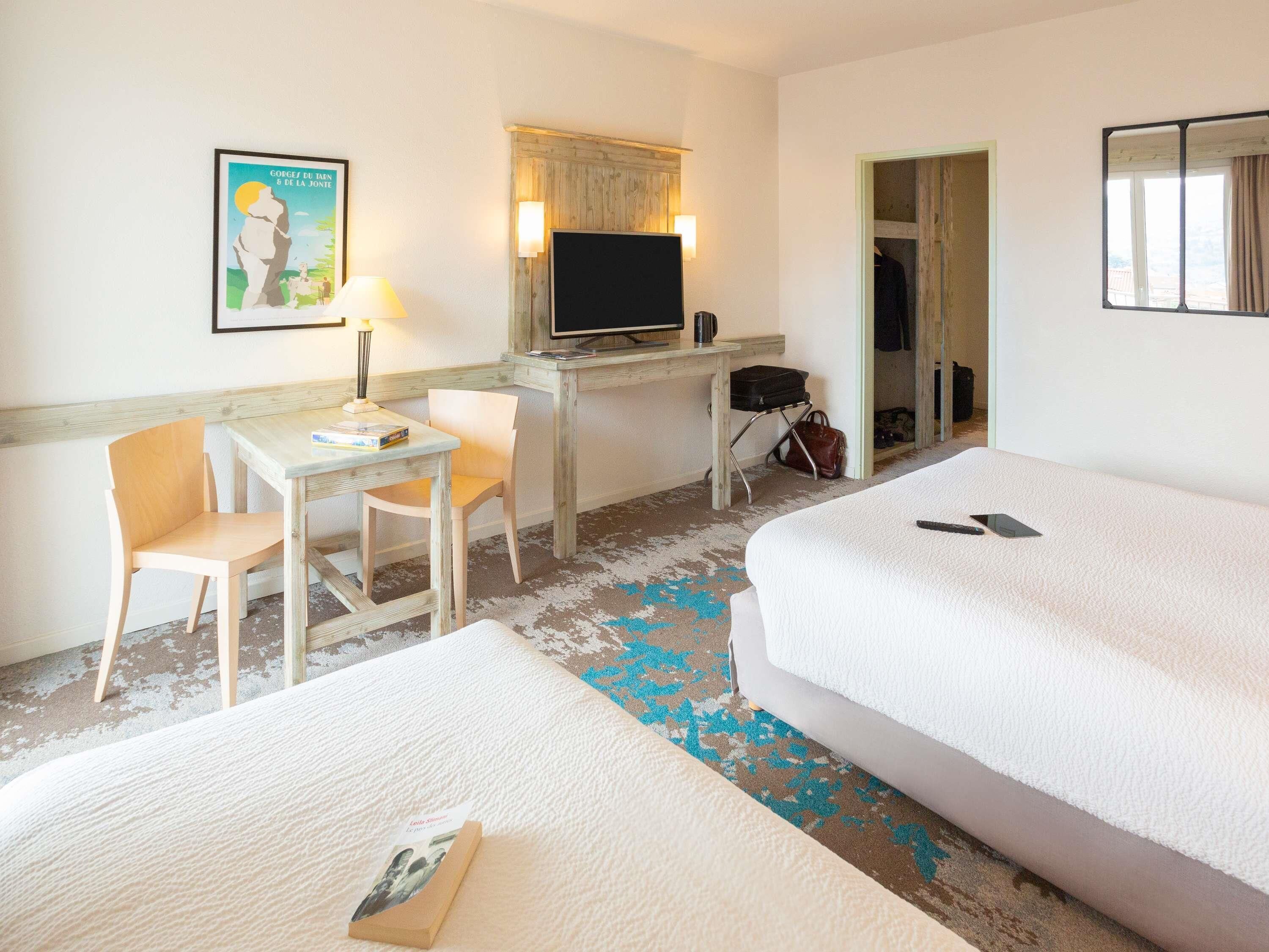 Une chambre d’hôtel avec un lit, un bureau et une chaise, une télévision et un tableau encadré au mur.