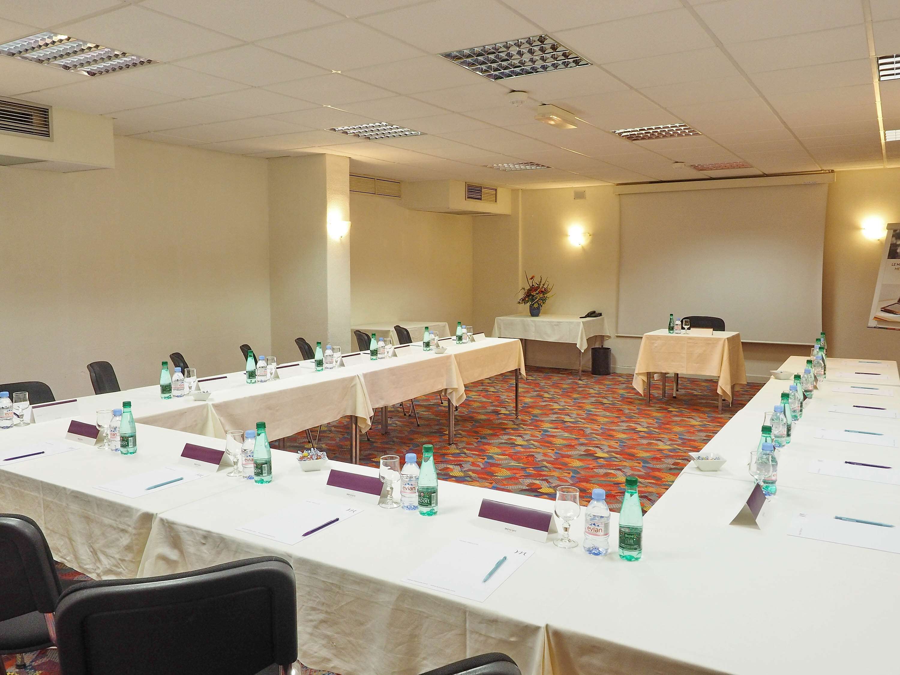 Un salón de conferencias con mesas largas, sillas, botellas de agua y tarjetas de identificación.