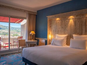 A hotel room with a large bed, a desk with a lamp, a chair, and a view of the outdoors. - Mercure Millau (Millau)