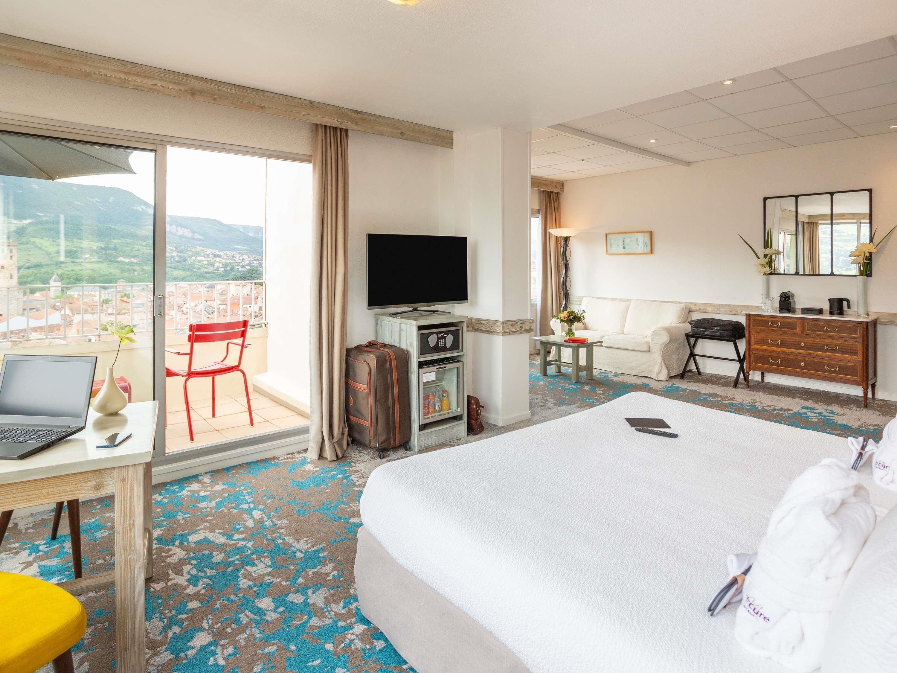 Habitación de hotel con cama, escritorio con ordenador portátil, televisor, cómoda y vista a la ciudad.