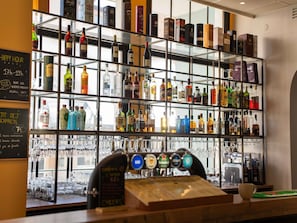 Un espace bar avec des étagères remplies de bouteilles d’alcool et un bar avec des robinets en évidence.