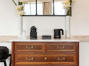 A wooden dresser with drawers, a black speaker, a white vase with flowers, and a black kettle on a marble countertop.