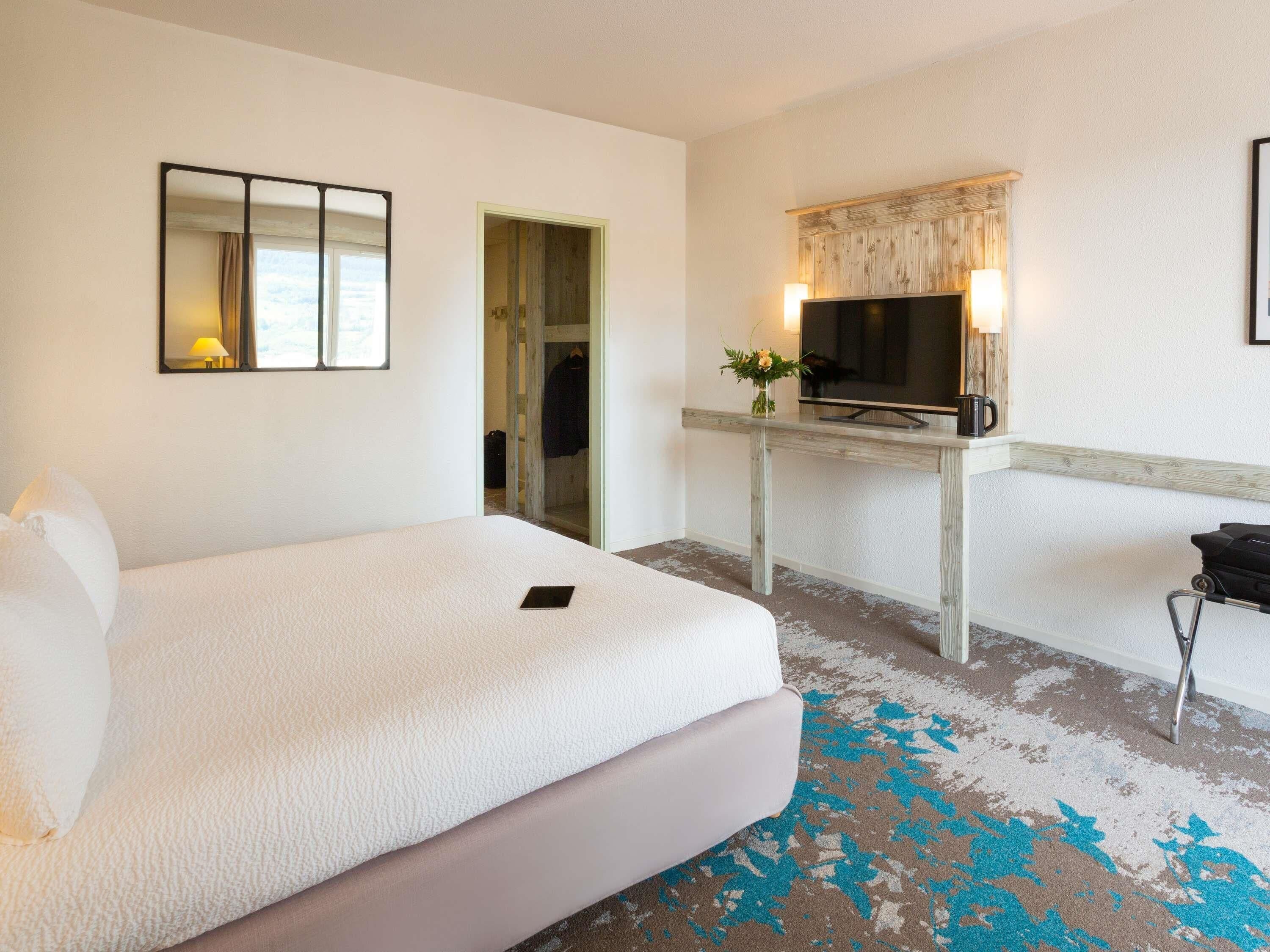 A hotel room with a large bed, a desk with a TV, and a mirror.