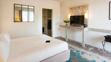 A hotel room with a large bed, a desk with a TV, and a mirror.