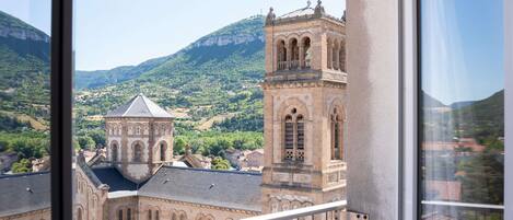 A view from a balcony overlooking a historic building with a bell tower, set against a backdrop of green hills and a clear sky.