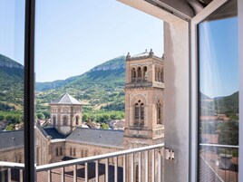 Vista desde un balcón que da a un edificio histórico con una torre de campanas, con colinas verdes y un cielo despejado de fondo.
