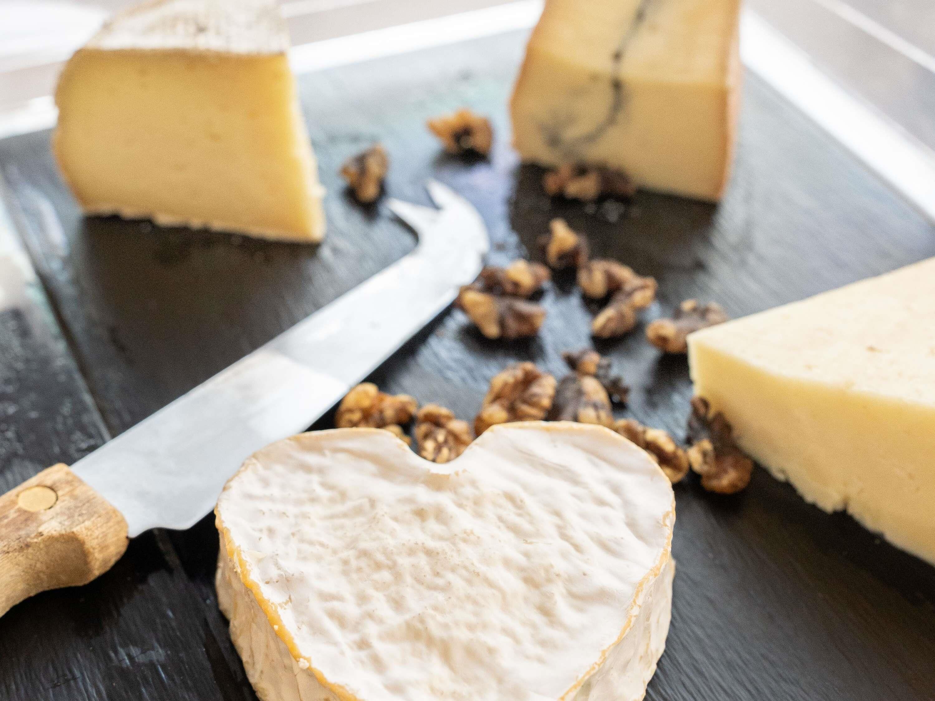 A cheese wheel with a knife and scattered nuts on a dark surface.