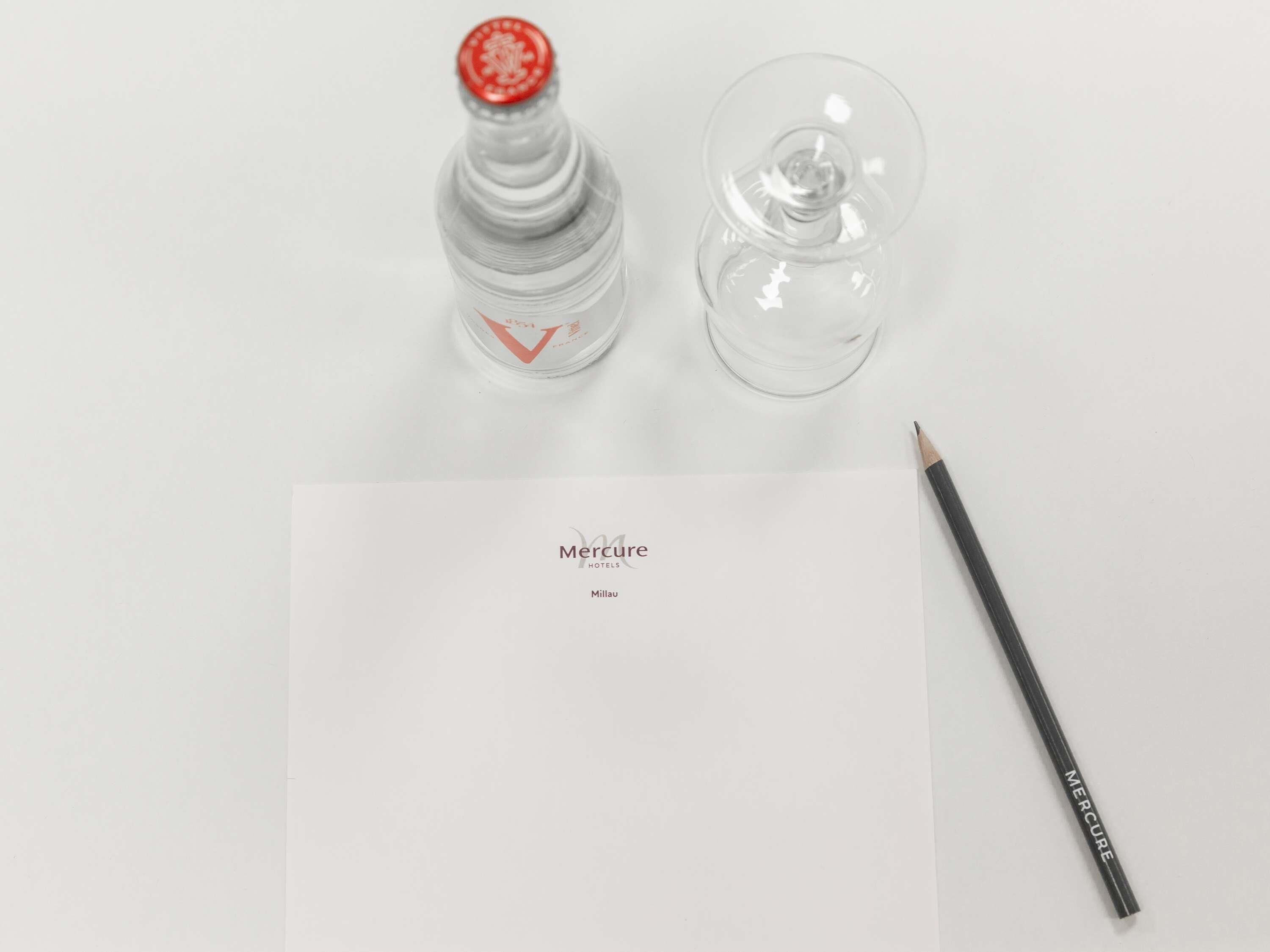 En flaske, et glas, en blyant og et stykke papir med teksten 'Mercure Hotels Millau'.