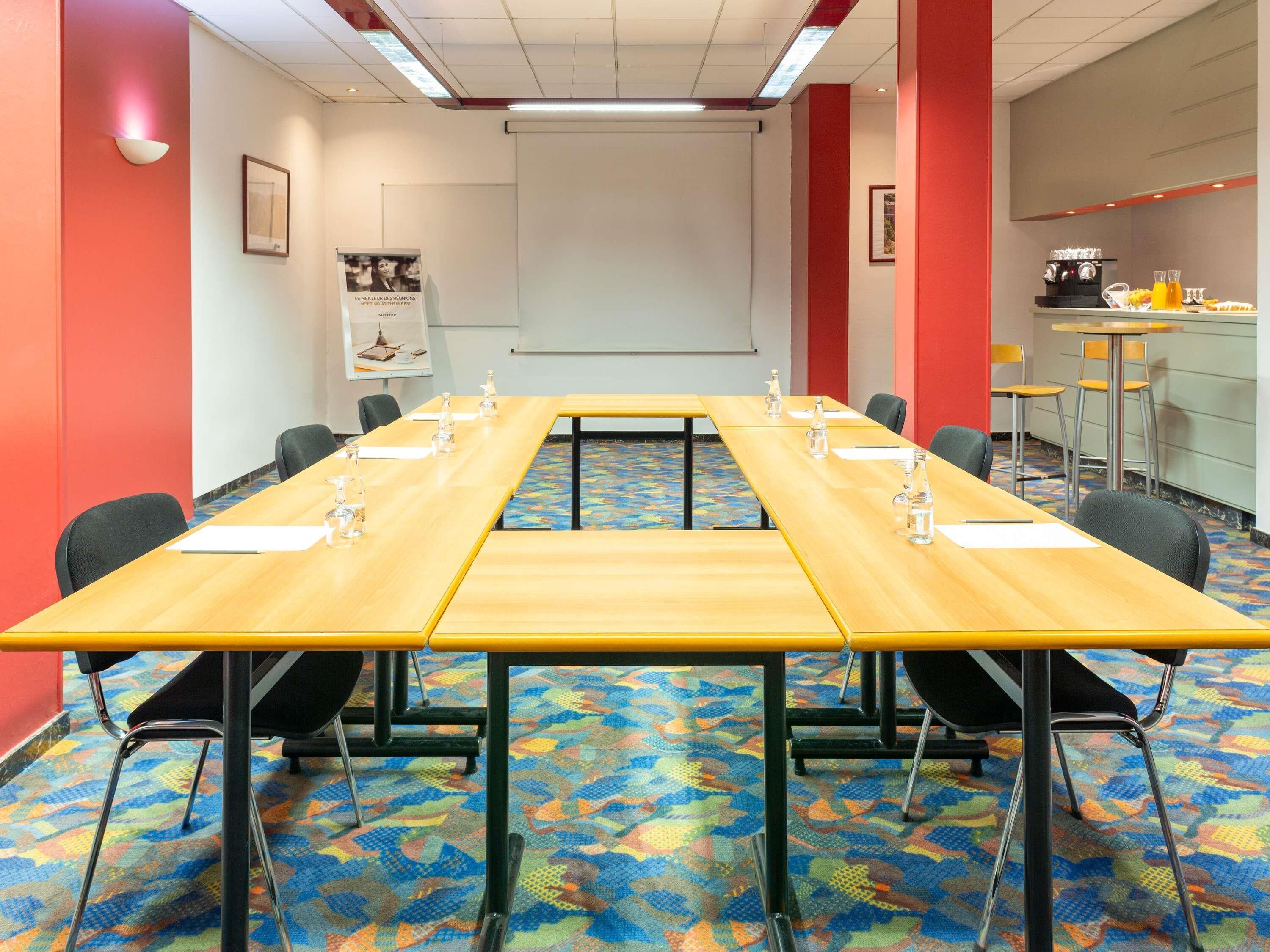 Ett konferensrum med ett långt bord, stolar, en projektorduk och en plats för att göra kaffe.
