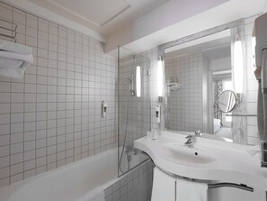 A modern bathroom with white tiled walls, a bathtub, a sink with a mirror, and a shower.