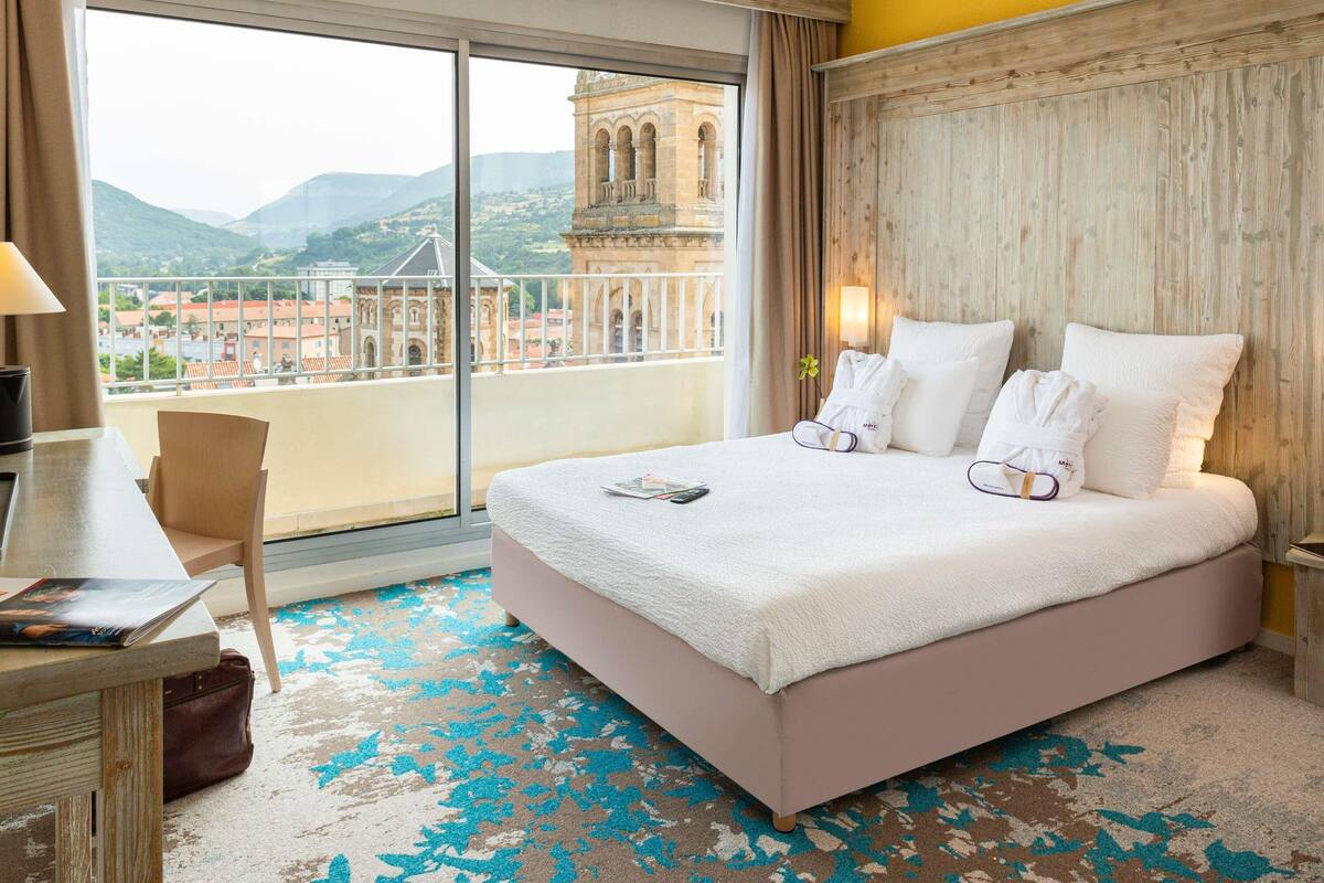 A hotel room with a large bed, a desk, a chair, and a view of a historic building.