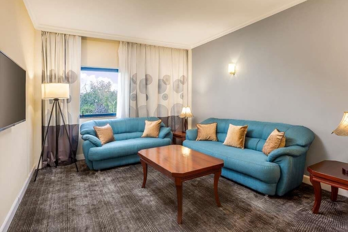 Habitación de hotel con sofá azul, una mesa de centro de madera, lámpara y vistas al exterior.