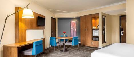 Ein Hotelzimmer mit Bett, Schreibtisch, Stuhl, Fernseher und Minibar.