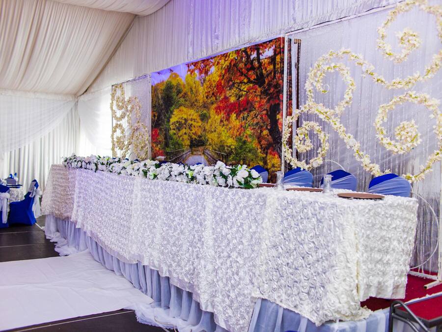A banquet hall with a long table covered in white lace, blue chairs, and floral decorations.