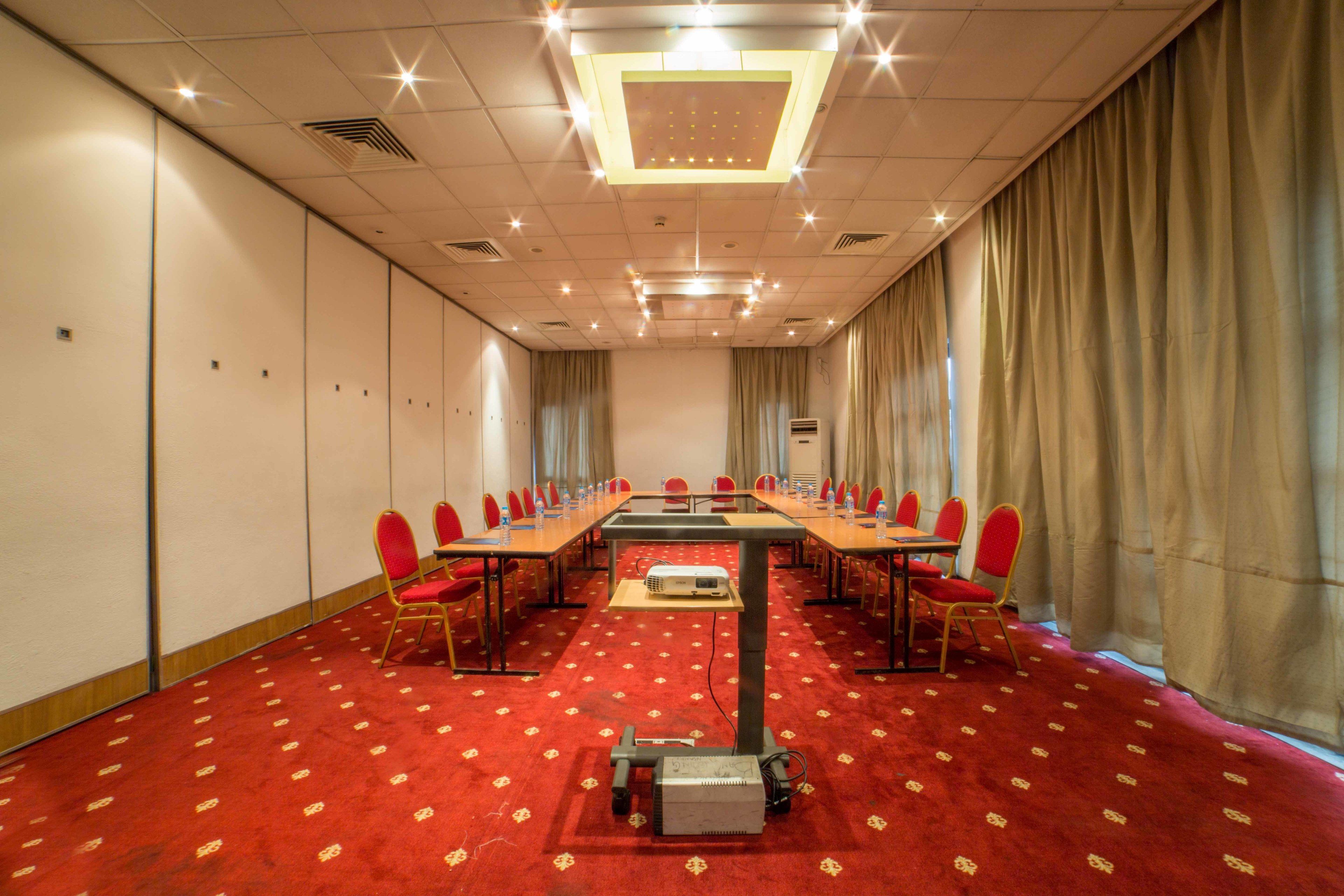 A conference room with a long table, red chairs, a projector, and a carpeted floor.